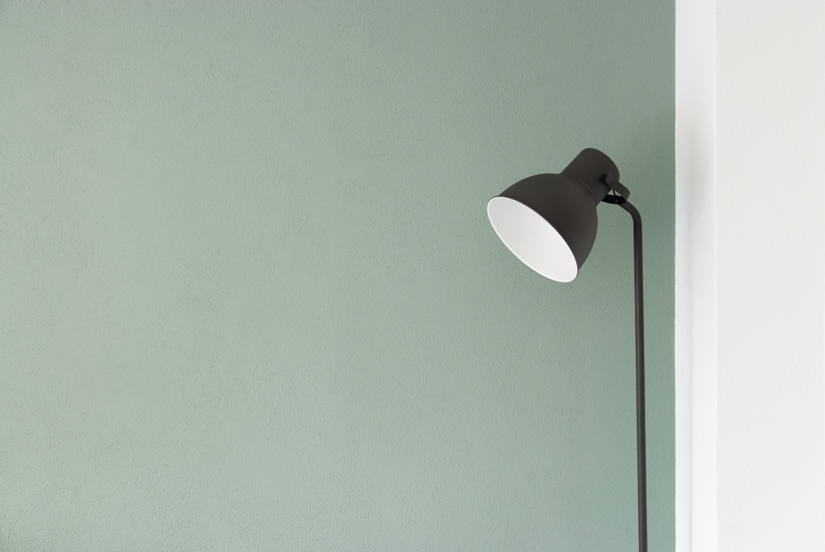 A real photograph of a desk lamp against a pale green wall.